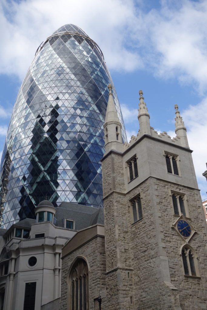 A modern glass building next to an old church in the city of London